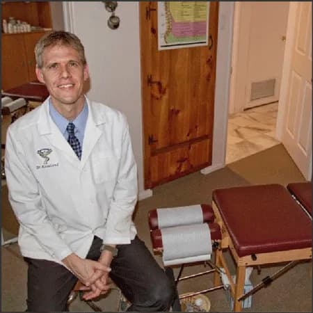 Dr. Erik Rosseland seated beside a chiropractic treatment table